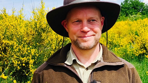 Eifelranger Sascha Wilden im Portrait, Ginsterbüsche im Hintergrund.