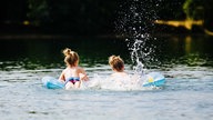 Zwei Kinder baden mit Luftmatratze in einem Badesee.