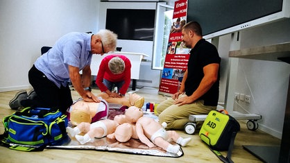 Uwe Blaschke und eine weitere Person üben Reanimationen an Puppen. Neben ihnen ein Mann, der sie dabei beobachtet.