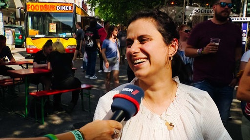 Eine Frau spricht in ein Mikrofon und lächelt dabei.