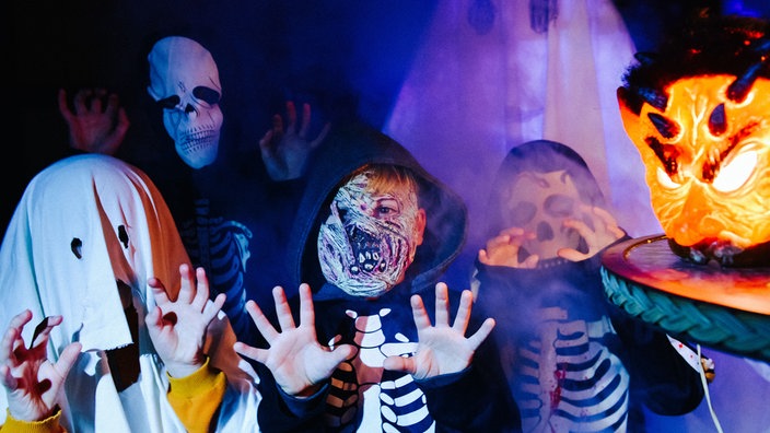Vier Kinder in Halloween-Kostümen machen einer Erschrecker-Pose in Richtung Kamera.