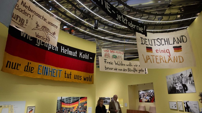 Blick in die neue Dauerausstellung im Haus der Geschichte in Bonn: In einem Raum hängen an gelben Wänden verschiedene Plakate mit Sprüchen, u.a. ein weißes auf dem steht "Deutschland einig Vaterland"