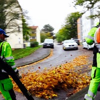 Mert Aybey und sein Kollege sind mit Laubbläsern an einer Straße in einem Wohngebiet unterwegs.