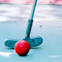 Roter Minigolf-Ball hinter dem ein Schläger zu sehen ist