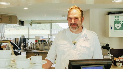 Frank Harnischmacher steht hinter der Café-Theke. Er lächelt.