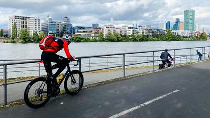 Frank Müller auf seinem Rennrad von der Seite. Im Hintergrund eine Uferszenerie in einer Großstadt.