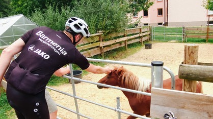 Frank Müller streichelt in Fahrradmontur ein braunes Pony an einem Gatter.