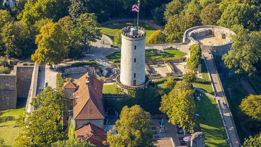 Luftaufnahme der Sparrenburg. Zentral steht ein großer Turm aus Stein, darum mehrere Häuser.