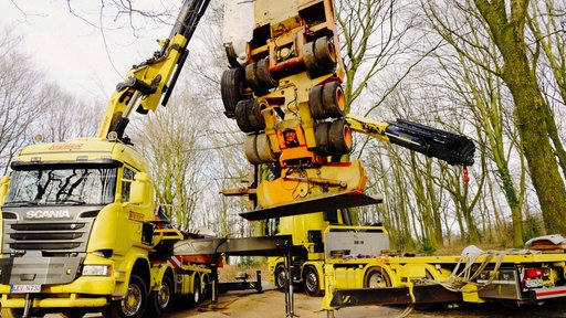 Zwei gelbe Kranwägen richten einen orangenen Lkw-Anhänger auf.