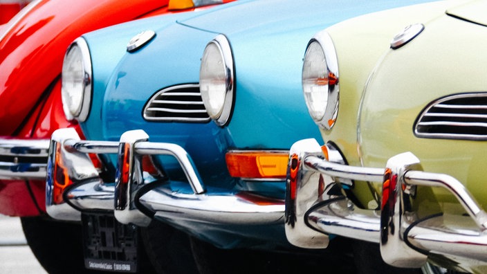 Ein roter, blauer und ein grüner VW Oltimer nebeneinander.