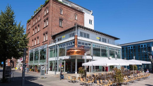 Das Backsteingebäude der Lindenbrauerei in Unna mit modernem gläsernen Anbau und Tischen und Stühlen davor
