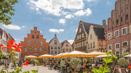 Rund um den Marktplatz in Warendorf stehen historische Giebelhäuser, auf dem Platz sitzen Menschen unter Sonnenschirmen