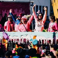 Ein Karnevalswagen. Die Frauen auf dem Wagen haben die Arme zum Jubel erhoben.