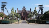 Man sieht die rot-geziegelte Zeche Zollern in der Mitte des Bildes. Rechts und Links daneben sieht man jeweils zwei Fördertürme. 