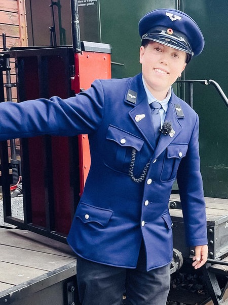 Leo steht stolz, gekleidet in seine Uniform, an einem historischen Eisenbahnwagon.