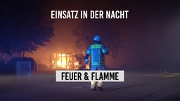 Ein Feuerwehrmann steht in der Nacht vor einem brennenden Gebäude