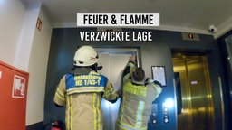 Zwei Feuerwehrmänner stehen vor einem Aufzug