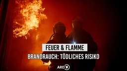 Zwei Feuerwehrmänner stehen im Dunkeln, Feuer breitet sich hinter ihnen aus