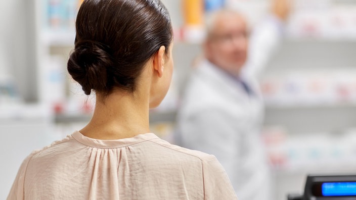 Das Beitragsbild des Dok5 "Gender und Race in der Medizin" zeigt eine stehende Frau von hinten in einer Apotheke. 