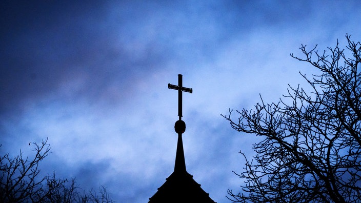 Dunkle Wolken ziehen über das Kreuz auf einer Kirche hinweg.