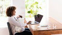 Das Beitragsbild des Dok 5 "Mütter im Job - Vereinbarkeit von Familie und Beruf" zeigt eine Mutter, die mit ihrem Säugling im Arm am Esstisch sitzt und am Laptop arbeitet. 