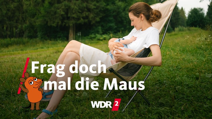 Lächelnde Frau sitzt in einem Campingstuhl auf einer Wiese und stillt ein Baby
