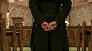 Das Beitragsbild des Dok5 "Vater unser – Das schwere Los der Priesterkinder" zeigt einen Priester in Soutane, der die Hände hinter dem Rücken verschränkt hält.