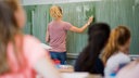 Eine junge Lehrerin schreibt Zahlen an eine Schultafel.