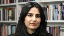 Die Schriftstellerin Karosh Taha steht vor einer Bücherwand.