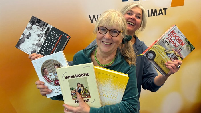Ulla Scholz und Heike Knispel stehen im WDR 4-Studio und halten fünf Kochbuchempfehlungen in den Händen