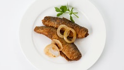 Zwei Brathering-Stücke sind mit Zwiebelringen und Petersilie auf einem Teller angerichtet