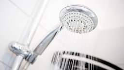 Ein Duschkopf hängt in einer Dusche in einem Badezimmer und es läuft Wasser aus ihm heraus.