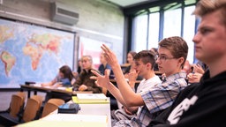 Schülerinnen und Schüler einer Oberstufen-Klasse sitzen im Klassenzimmer und blicken Richtung Lehrkraft. 