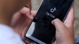 Jemand hält ein Smartphone in den Händen, auf dem TikTok geöffnet ist