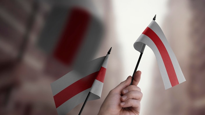 Menschen halten kleine belarussische Flaggen (rot-weiß) in der Hand