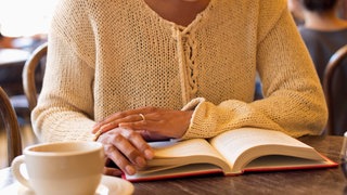 Symbolbild Offline Café: Eine Frau hält liest ein Buch in einem Café.