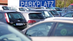 Ein überdimensionales Schild "Parkplatz" hängt an einer Parkfläche für Pkw.