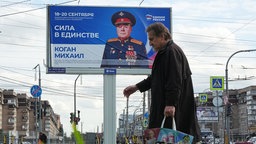 5.09.2026, Russland, St. Petersburg: Ein Mann geht an einer Plakatwand vorbei, auf der dazu aufgerufen wird, für einen Kandidaten der Partei "Einiges Russland" für das Kommunalparlament zu stimmen.
