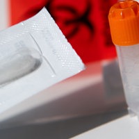 Ein Wattestäbchen und zwei Röhrchen für biologische Proben von einem DNA-Test zur Ahnenforschung stehen auf einem Tisch.