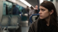 Eine junge Frau sitzt mit ängstlichem Gesichtsausdruck in einem Bus