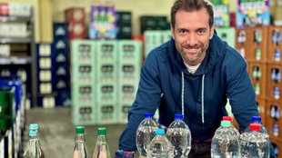 Daniel Aßmann steht in einem Getrränkeladen und lächelt in die Kamera.