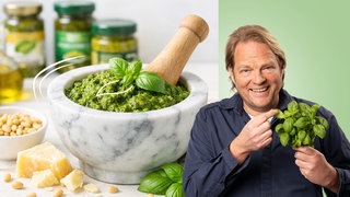 Björn Freitag hält Basilikum in der Hand. Im Hintergrund ist Pesto zu sehen. 