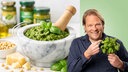 Björn Freitag hält Basilikum in der Hand. Im Hintergrund ist Pesto zu sehen. 