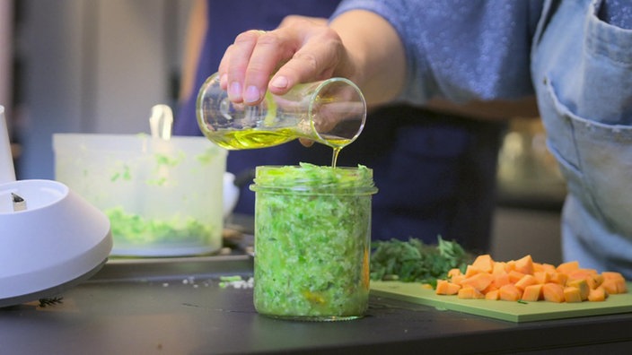 Das Bild zeigt ein Gefäß mit dem Grünen Pesto. Es wird Olivenöl draufgeschüttet.