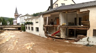 Ein übertretener Fluss und ein Haus, dessen eine Hälfte komplett weggerissen wurde.