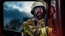 Ein Feuerwehrmann der Berufsfeuerwehr Duisburg in Schutzkleidung und abgelegter Atemschutzmaske steigt in ein Einsatzfahrzeug ein.