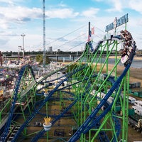 Menschen sitzen in einem Wagen auf einer Achterbahn bei der Rheinkirmes Düsseldorf. Im Hintergrund ist der Rhein zu sehen.