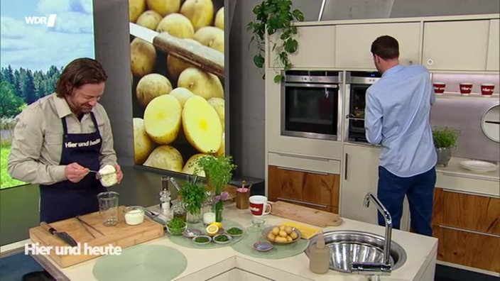 Olaf Baumeister und Moderator Sven Kroll stehen an der Küchenzeile im Hier und Heute Studio während sie kochen