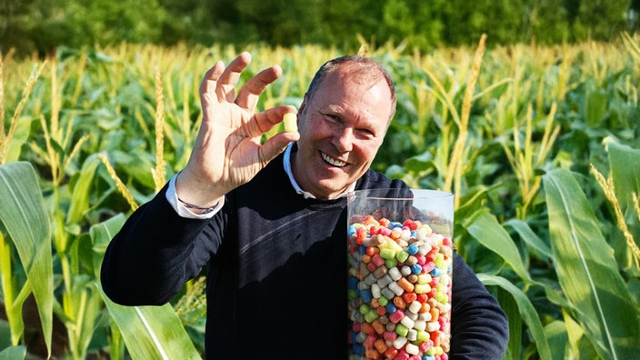 Landwirt Hubert Loick steht vor einem Maisfeld und hält ein großes Glas mit PlayMais in den Händen.