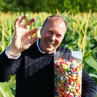Landwirt Hubert Loick steht vor einem Maisfeld und hält ein großes Glas mit PlayMais in den Händen.